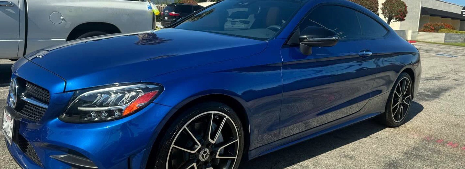 A blue Mercedes CLX receives luxury vehicle mobile detailing from Armando King Mobile Detailing near a white truck.
