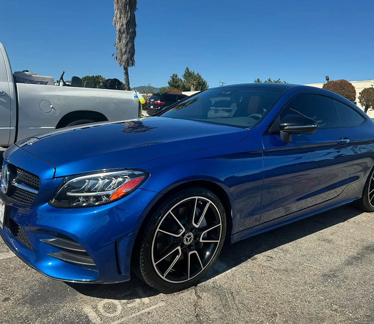 A blue Mercedes CLX receives luxury vehicle mobile detailing from Armando King Mobile Detailing near a white truck.